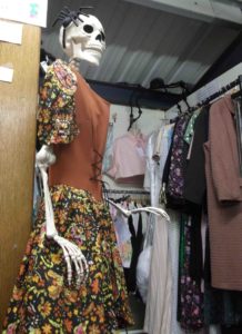 Full size skeleton in a 1970s dress in front of stall with new stock