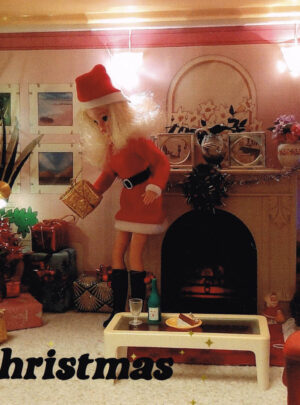 A Sindy doll ina Santa outfit places a present beneath a miniature Christmas Tree - 1970s text states Merry Christmas