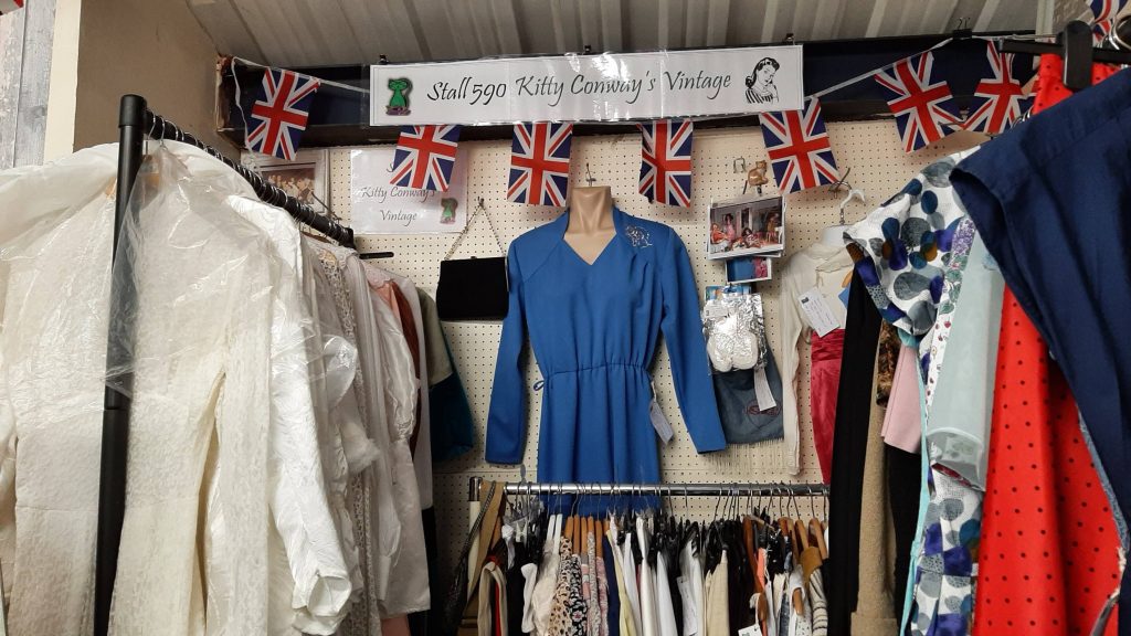 Stall 590 Kitty Conway's Vintage rails of clothing with a blue dress and bunting along the far wall